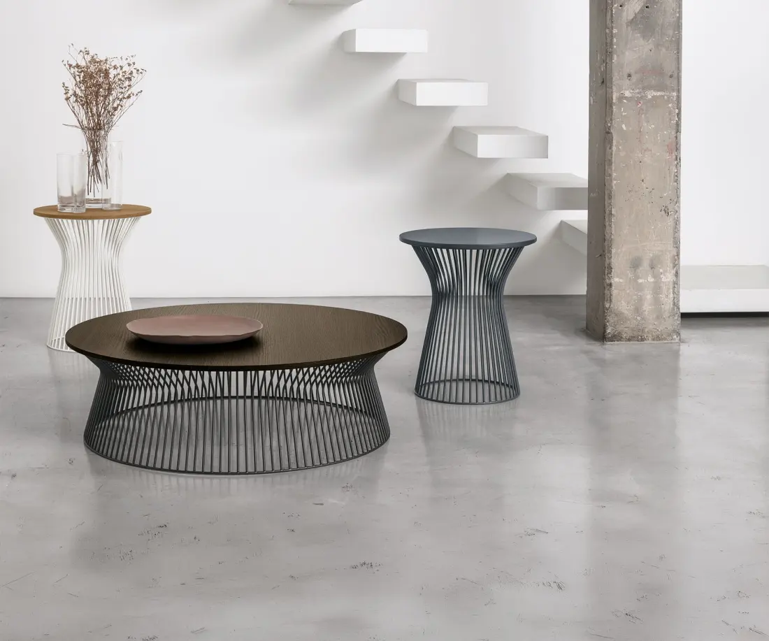 Tavolino e sgabello da salotto con struttura in filo metallico e piano tondo, su pavimento in cemento