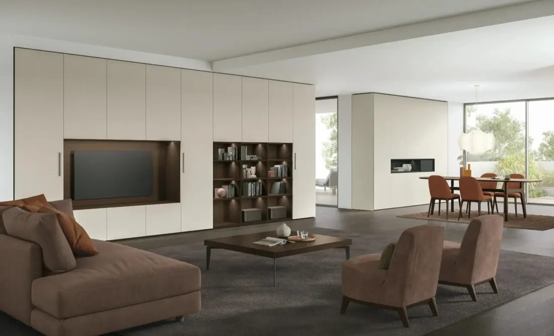 Zona giorno con parete attrezzata chiara, libreria a giorno e divano con chaise longue, aperta sulla sala da pranzo