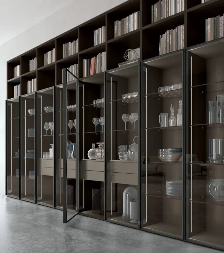 Libreria Atlante a tutta parete con ante in vetro fumé, libri sui ripiani alti e servizio di bicchieri in mostra