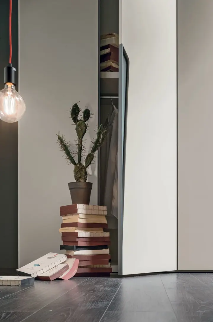 Angolo di cameretta con anta dell'armadio socchiusa, lampada a sospensione e libri impilati