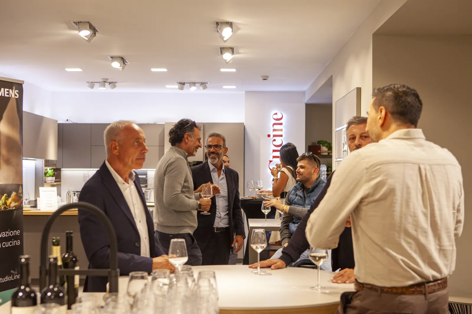 Ospiti in conversazione attorno al tavolo dell’aperitivo, fra le composizioni montate