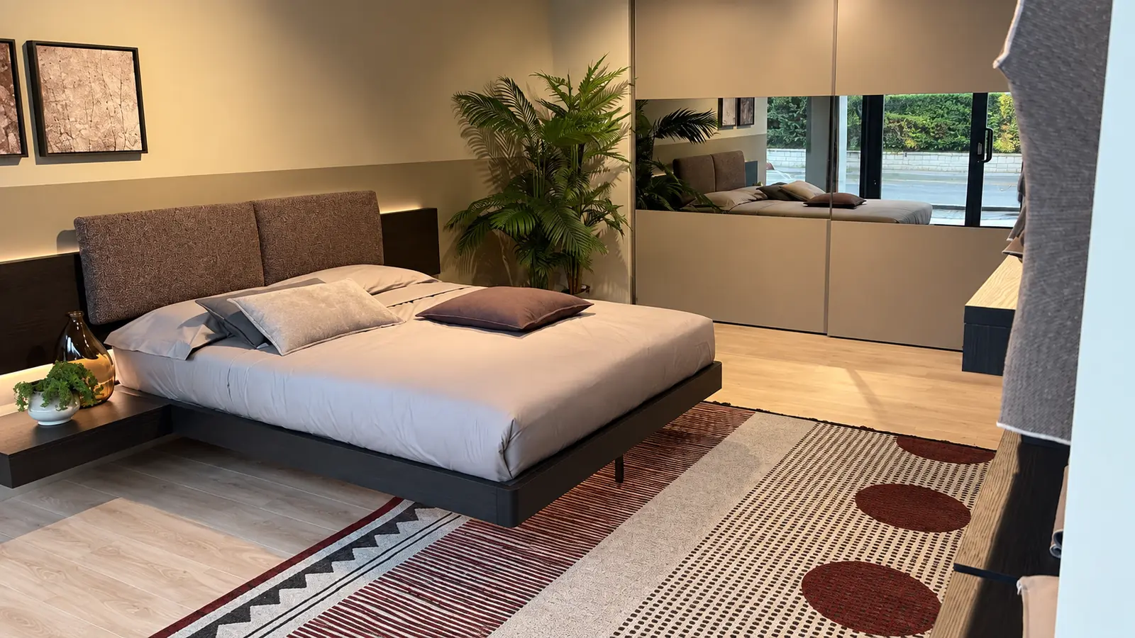 Allestimento della zona notte nello showroom di Manno, con letto imbottito e armadio a specchio