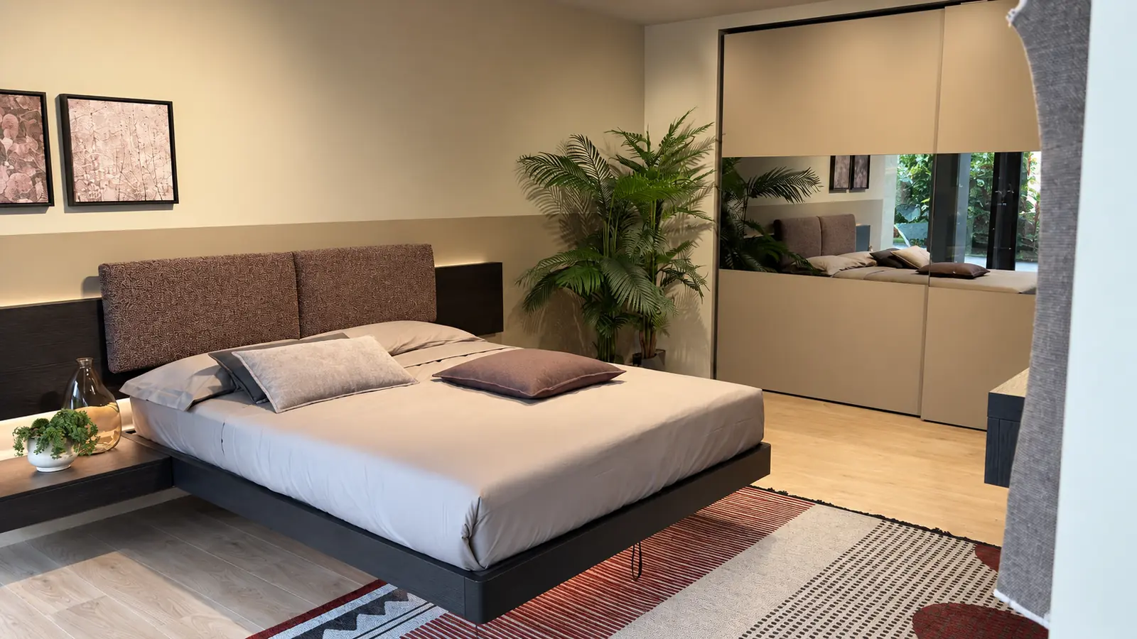 Camera da letto dello showroom con letto imbottito, quadri alla parete e armadio a specchio
